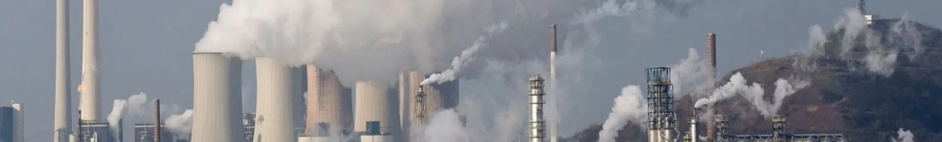 Numerous cooling towers and chimneys are emitting white plumes.