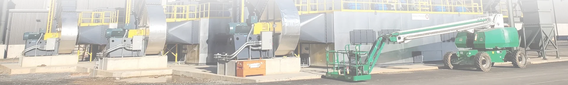 An articulated boom lift parked beside a fan and a chimney.