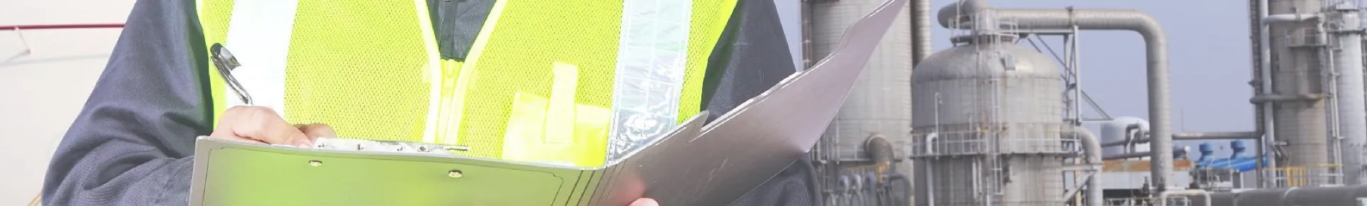 An employee is writing with a pen in front of industrial equipment.